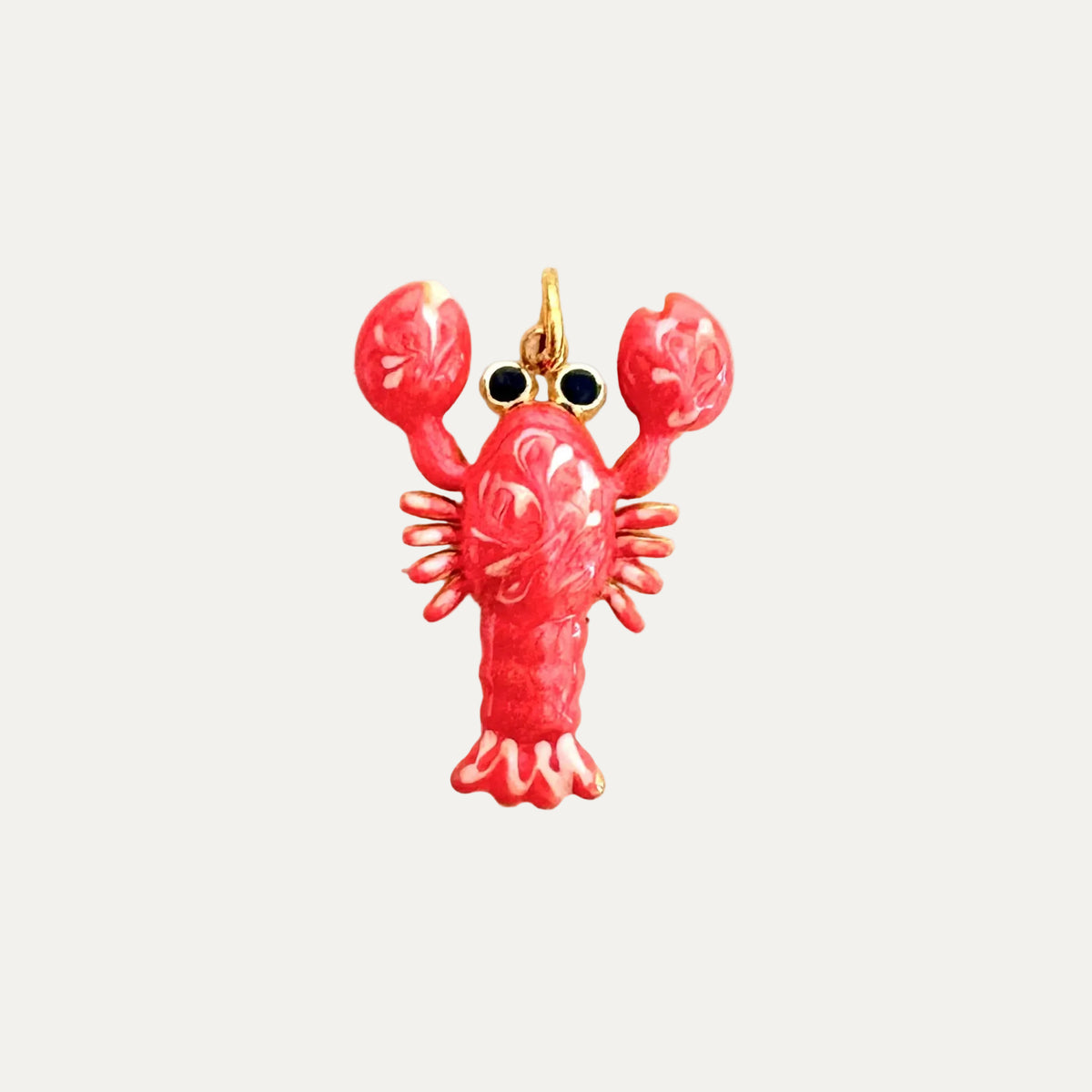 A lobster-shaped charm or pendant with a glossy pink-red enamel body, gold-tone metal outlines, and small black eye details, centered on a plain off-white background.