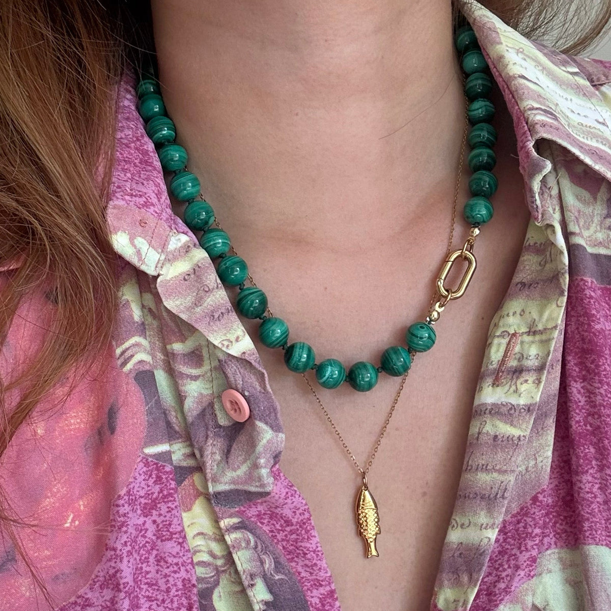 Person wearing a green beaded necklace with a gold fish pendant on a patterned shirt.