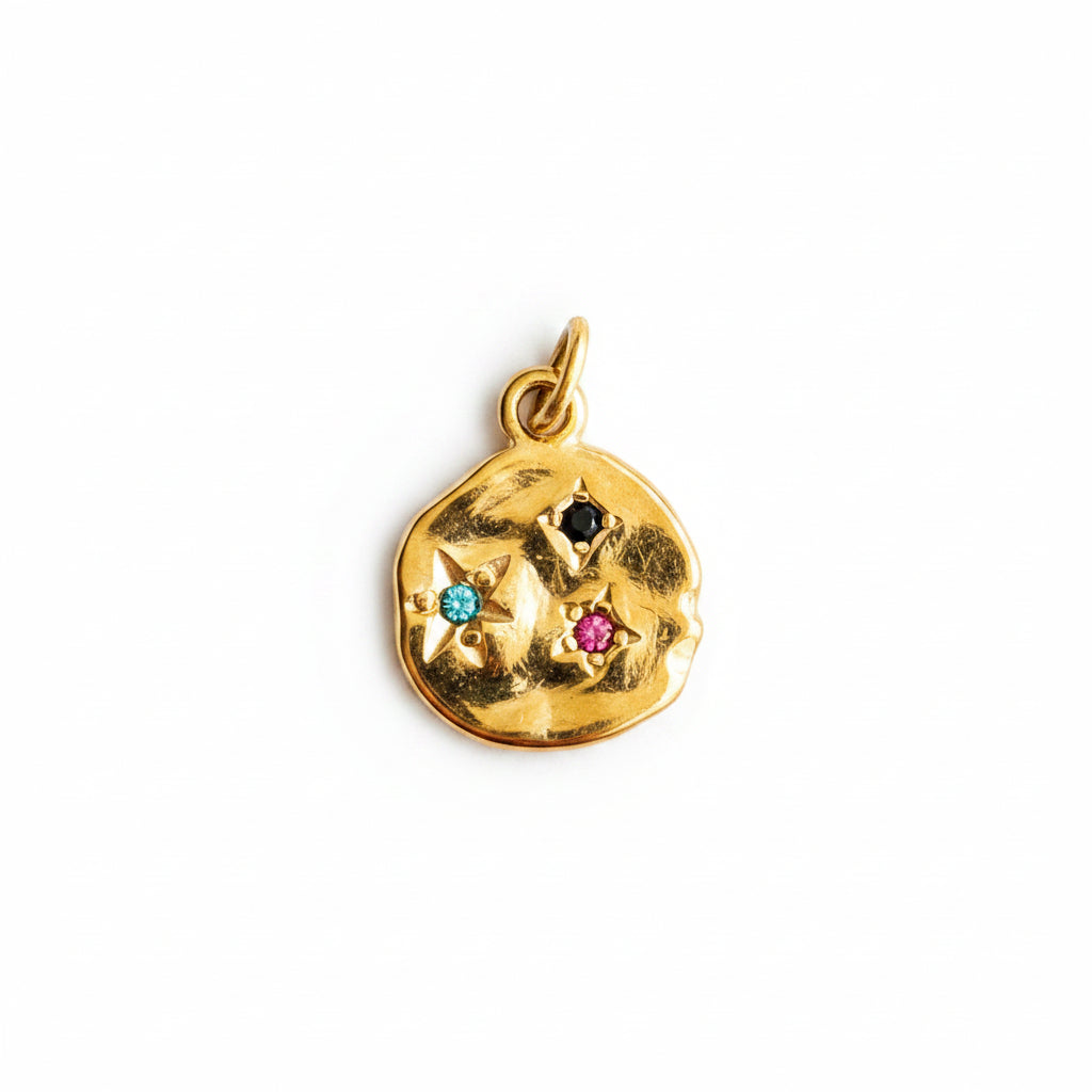 A gold-toned irregularly shaped pendant charm featuring three small star motifs set with colorful gemstones in black, turquoise blue, and pink, shown on a plain white background.