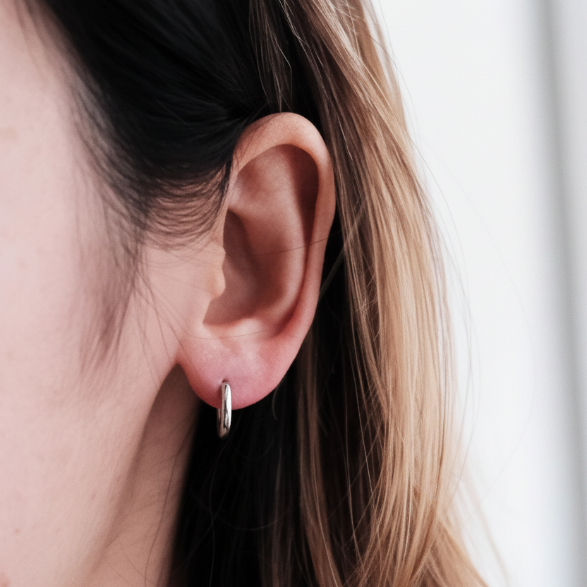 A close-up of a person's ear wearing a small, thin silver hoop earring.