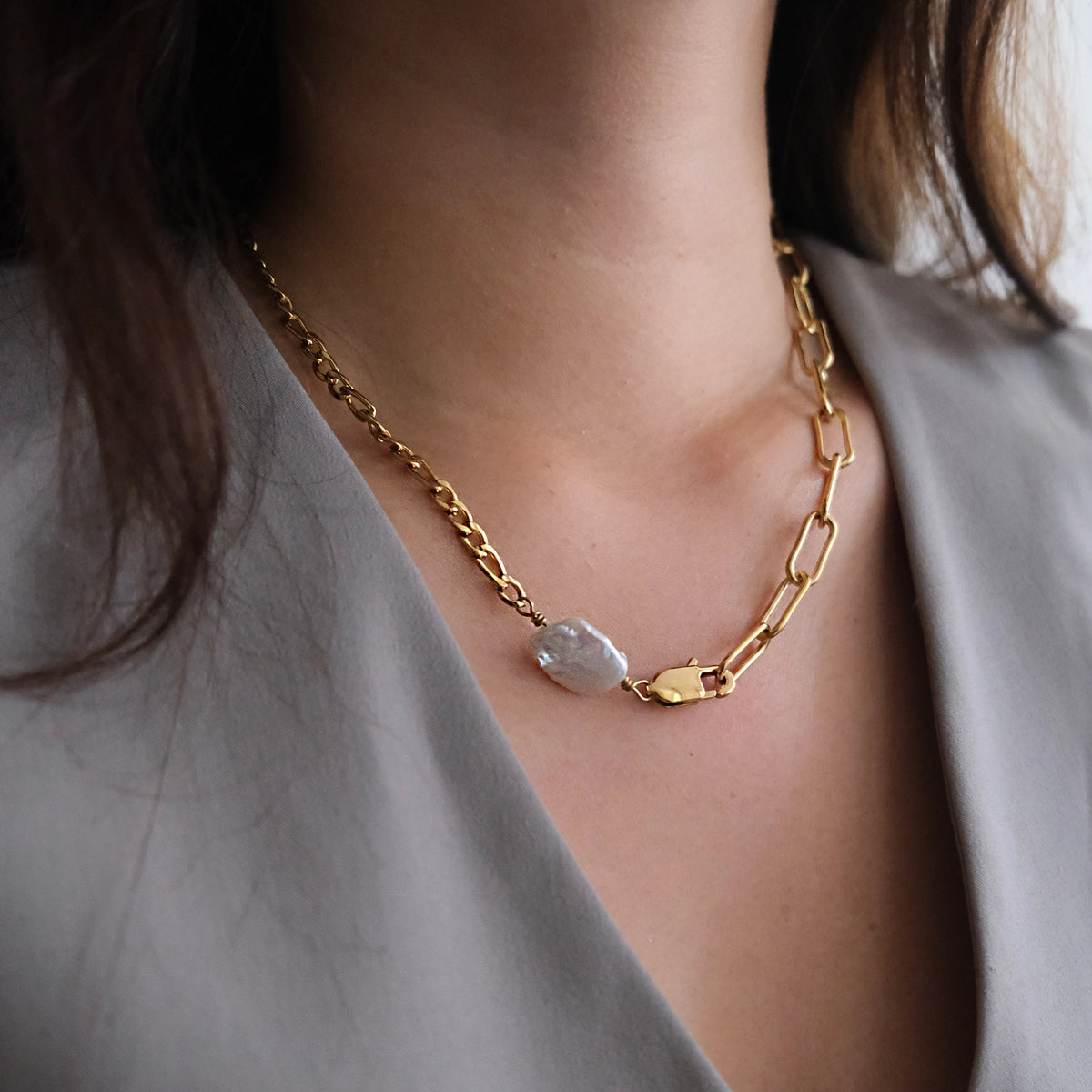 A close-up of a person wearing a gold chain necklace with a unique irregular white stone pendant, styled with a light gray top.