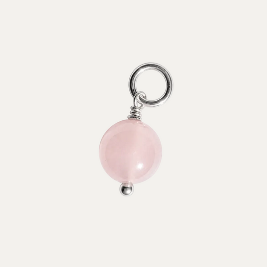 A rose quartz charm featuring a smooth, polished pink spherical bead suspended from a silver-colored metal ring and wrapped with a small silver coil, set against a plain white background.