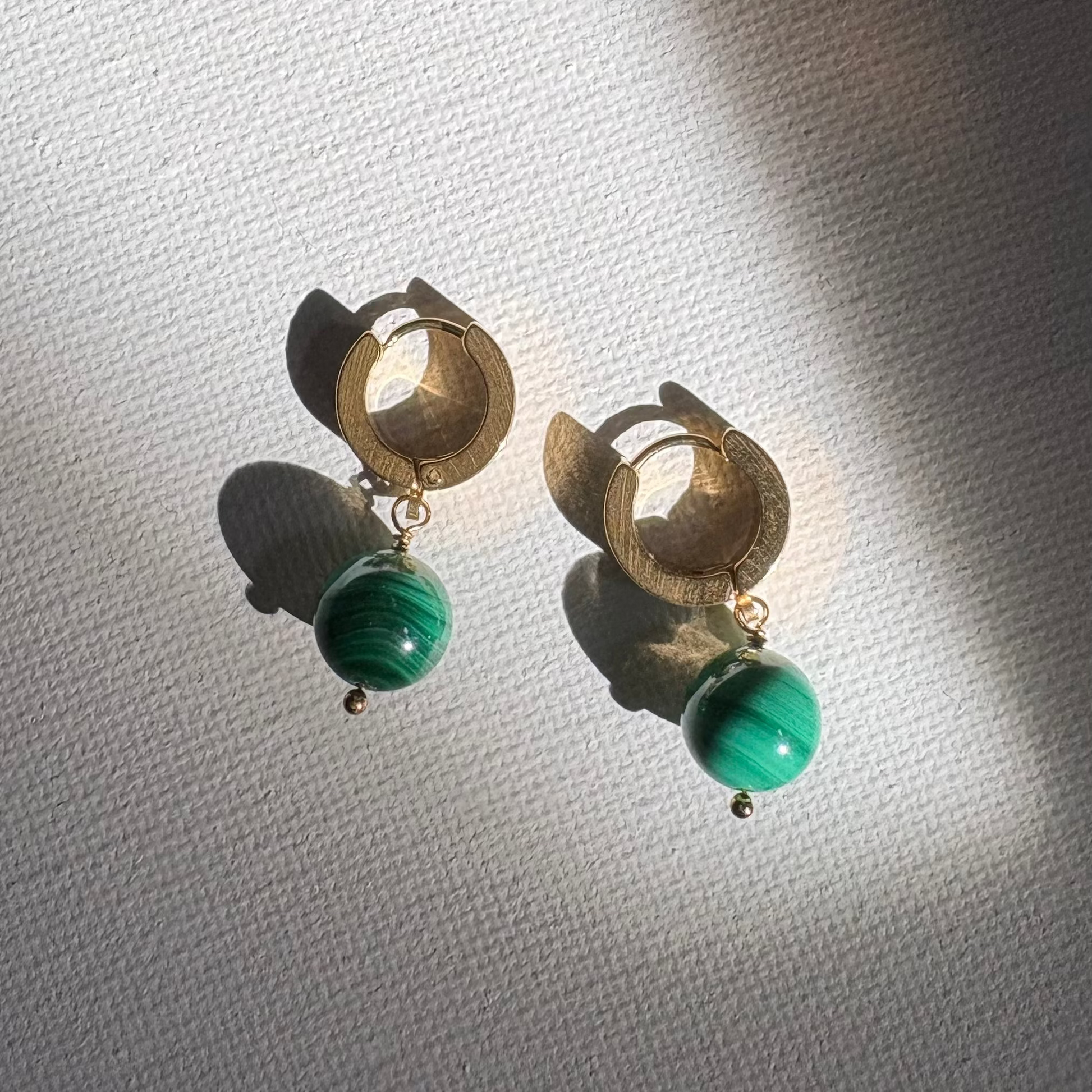 Gold hoop earrings with green beads on a textured white background