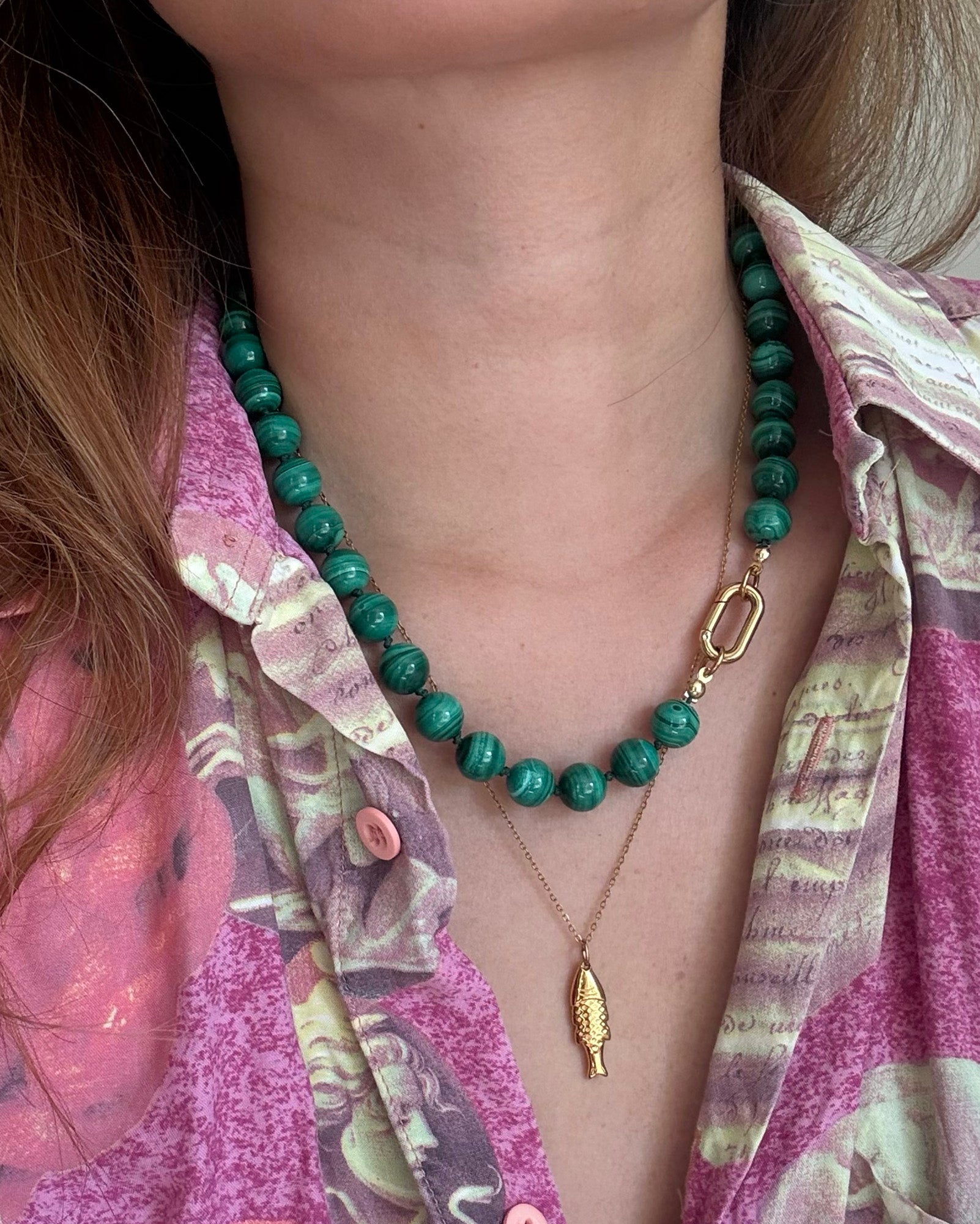 Person wearing a green beaded necklace with a gold fish pendant on a patterned shirt.