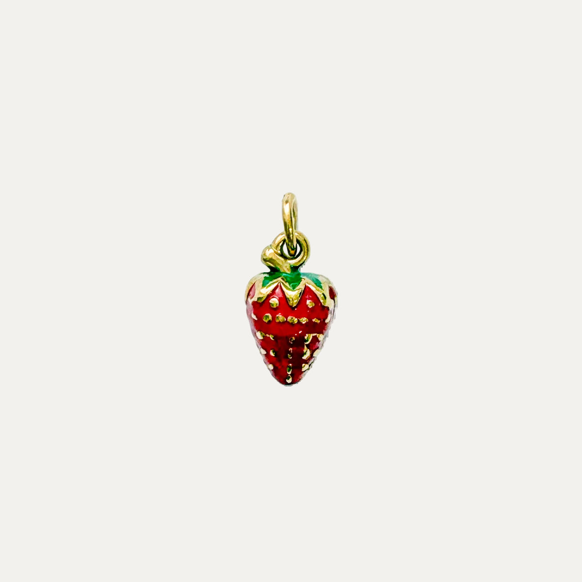 A small strawberry-shaped charm pendant with a gold-tone metal outline, red enamel body, and green leafy top, centered on a plain white background.