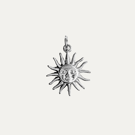 A silver sun pendant charm with a detailed face and radiating rays, shown on a plain white background.